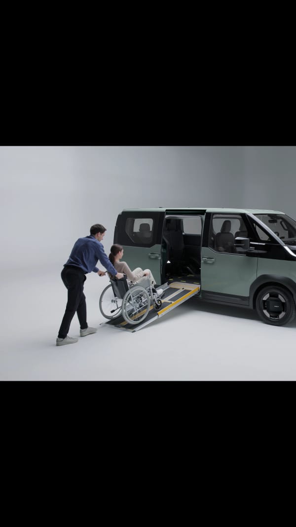 Rollstuhlfahrer wird mithilfe einer eingebauten seitlichen Rampe in einen Kia PV5 WAV geholfen, die sich sauber unter dem Fahrzeugboden verstauen lässt.